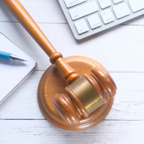 A brown wooden gavel lies between a white laptop and a notebook and pen.